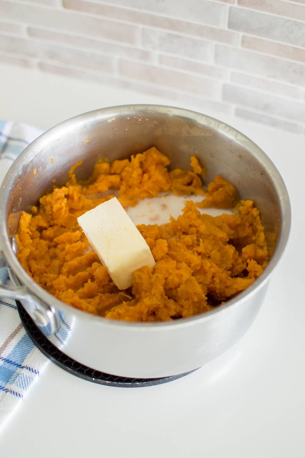 Adding butter and milk to a saucepan filled with mashed sweet potatoes