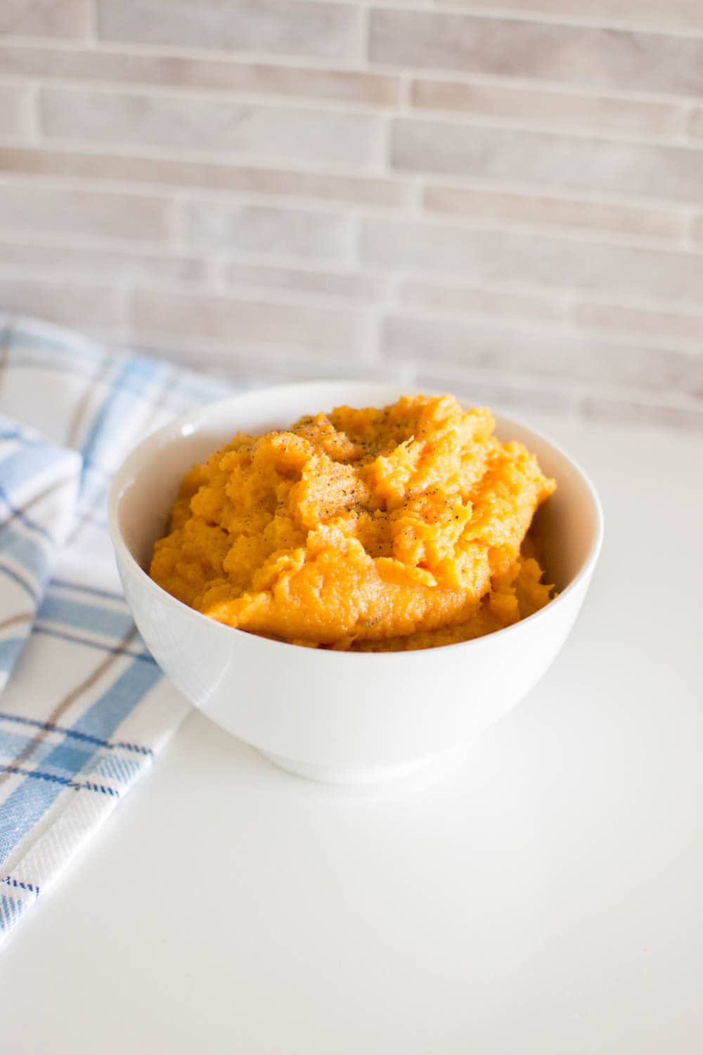 Mashed sweet potatoes with cracked black pepper, served in a white bowl
