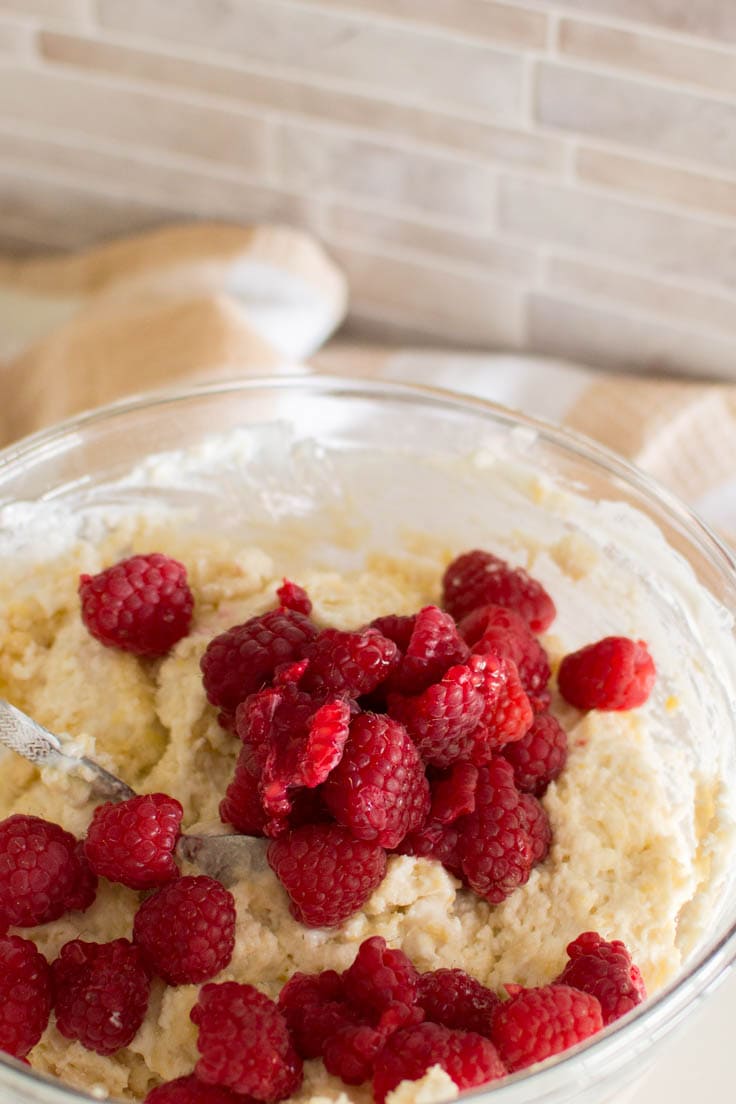 Adding raspberries to muffin batter in a glass bowl