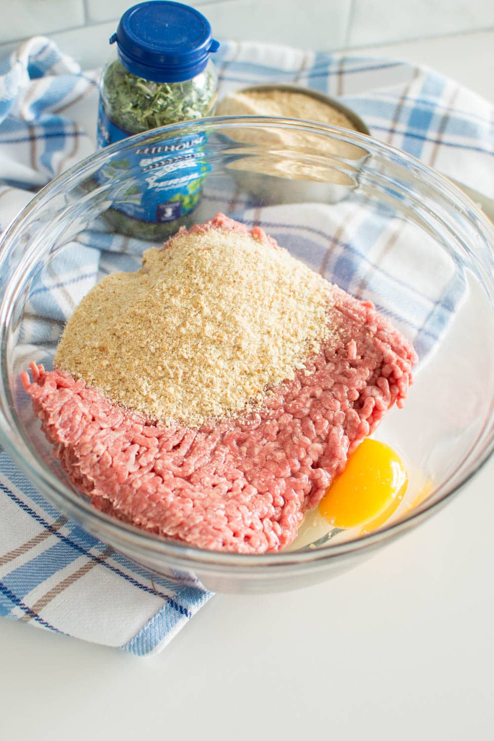 Raw ground beef with breadcrumbs and an egg in a large glass bowl