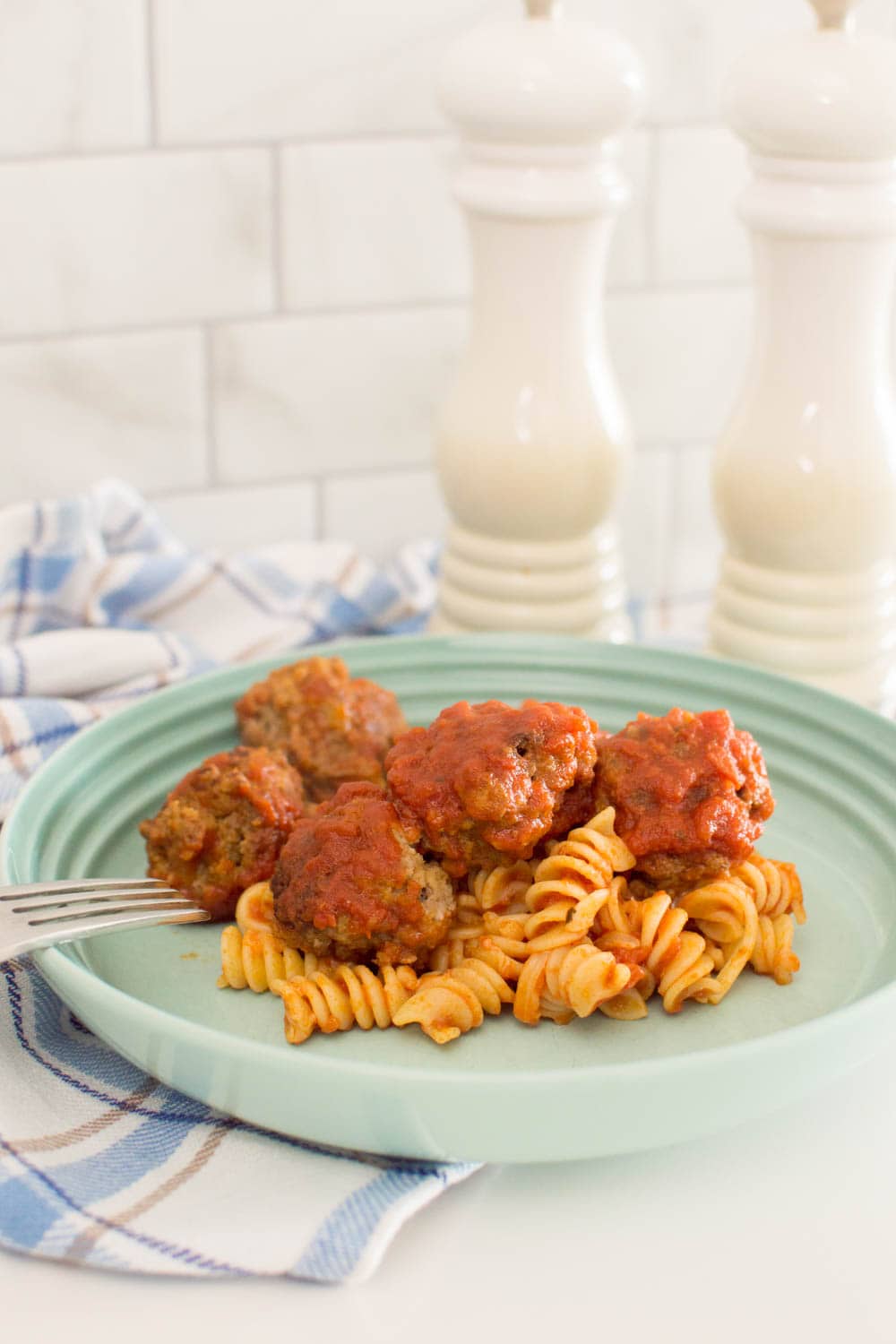 Basic homemade meatballs sitting on a bed of pasta in a turquoise pasta bowl