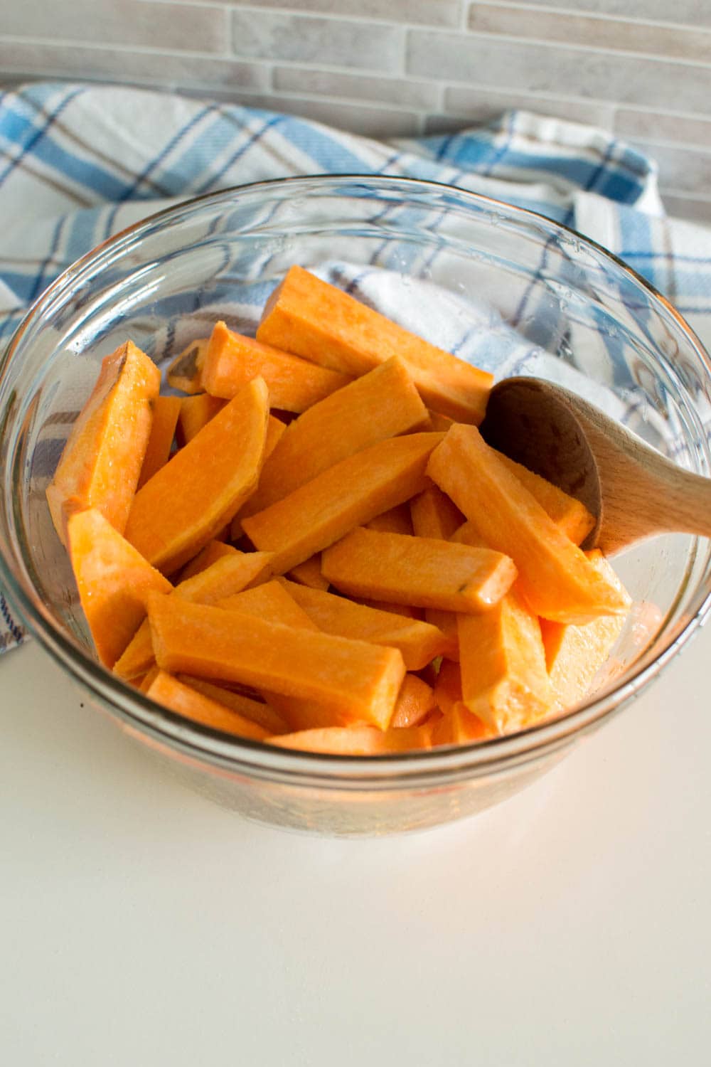 Slices of sweet potato in a glass bowl, coated with extra virgin olive oil and salt