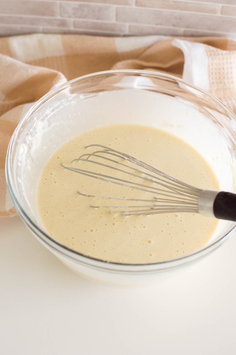 Waffle batter in a glass bowl, being mixed by a whisk
