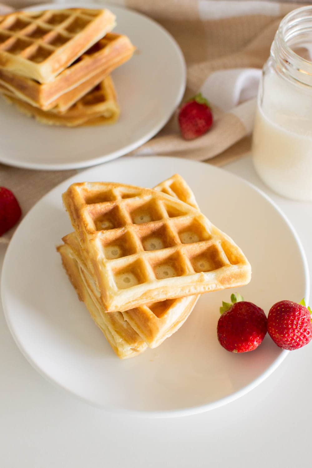 Easy homemade waffles cut into quarters and piled on top of one another being served on a white plate with fruit on the side