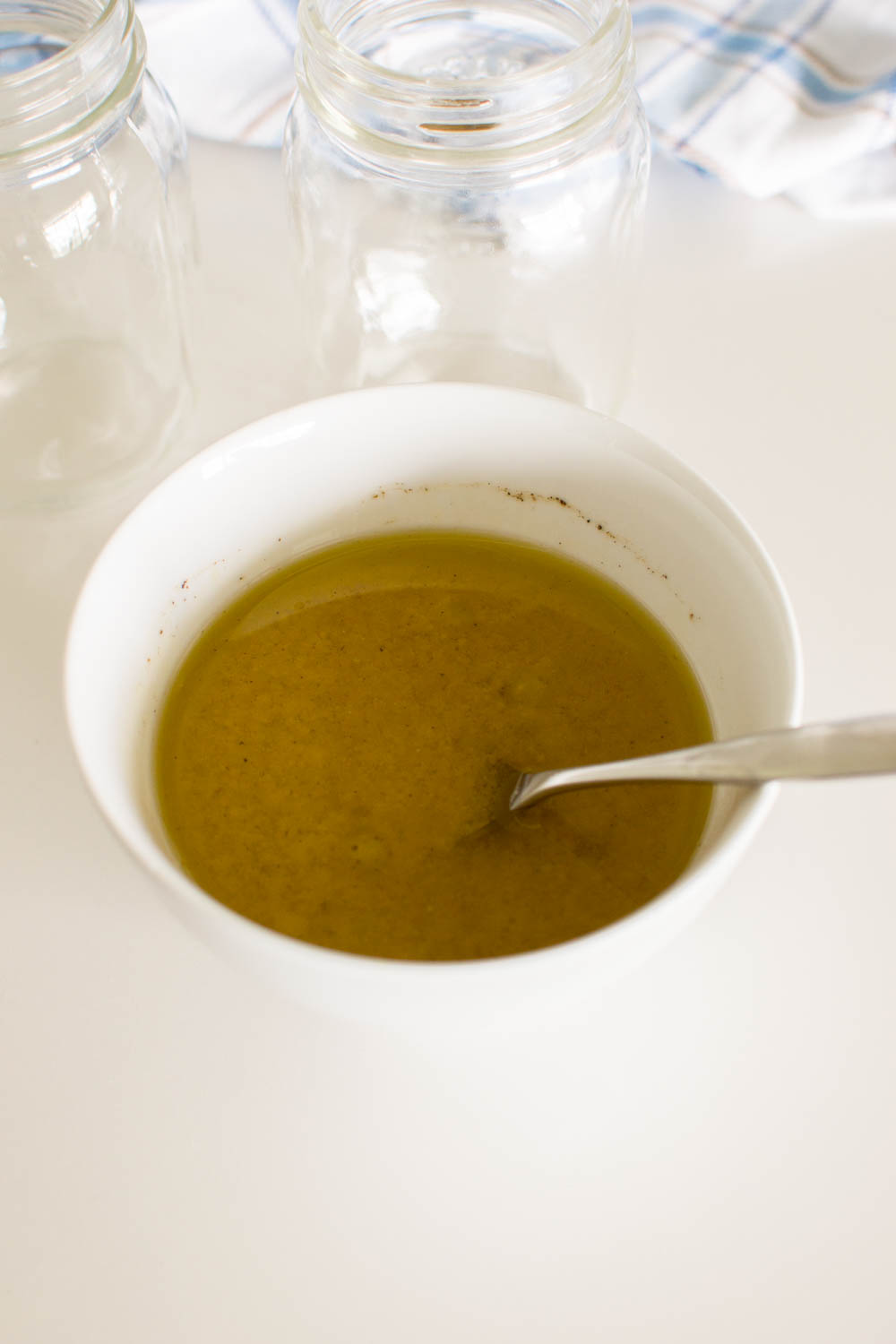Olive oil dressing in a white bowl being mixed with a small spoon