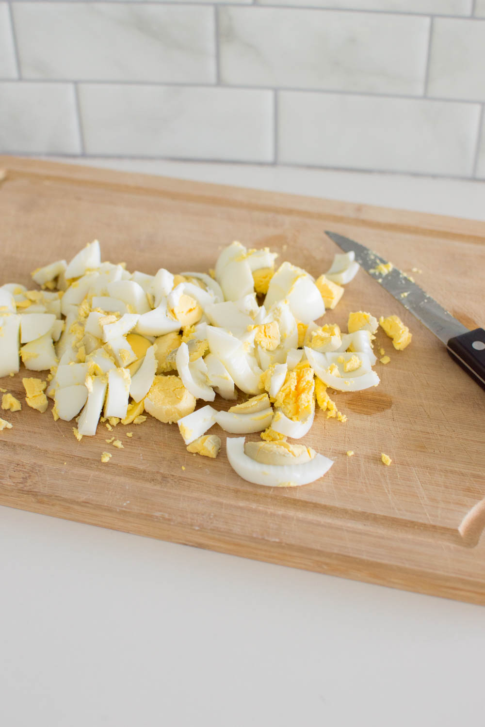 Hard boiled egg being chopped from on a wooden cutting board