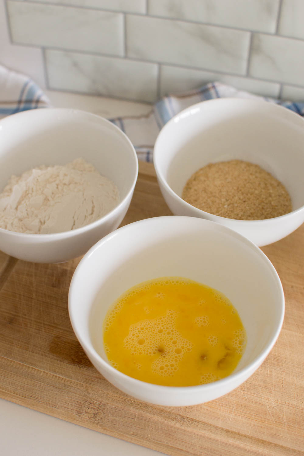 Egg wash, flour and bread crumbs each in their own white bowls