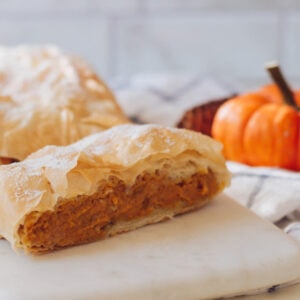 Pumpkin pie pastry on a cutting board with a slice cut from one end.