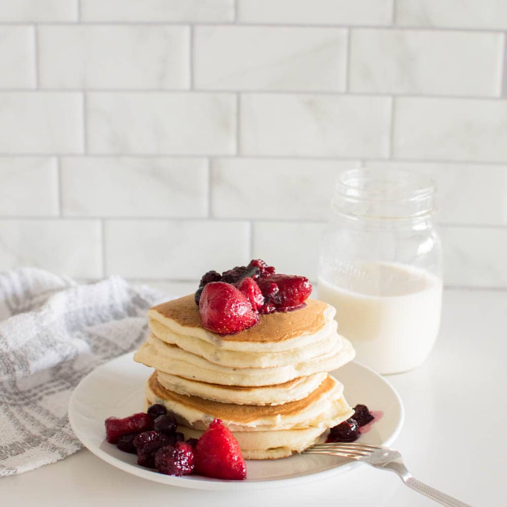 A stack of our delicious and easy homemade pancakes, topped with berry compote, sitting on a white plate and a fork