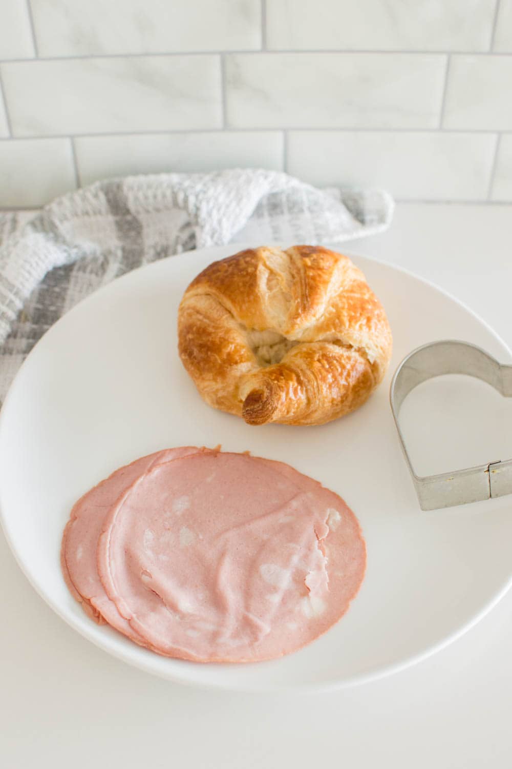 Luncheon meat, a croissant and a cookie cutter sitting on a white plate