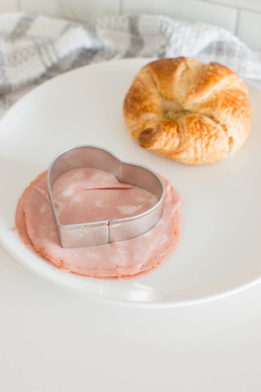 Cutting into a stack of luncheon meat on a white plate with a heart-shaped cookie cutter