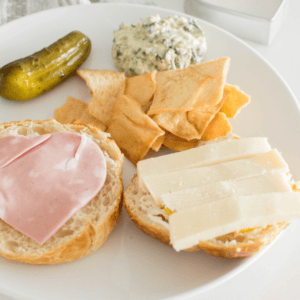 A cookie cutter slider with heart-shaped luncheon meat, open faced and accompanied by crackers, dip and a pickle