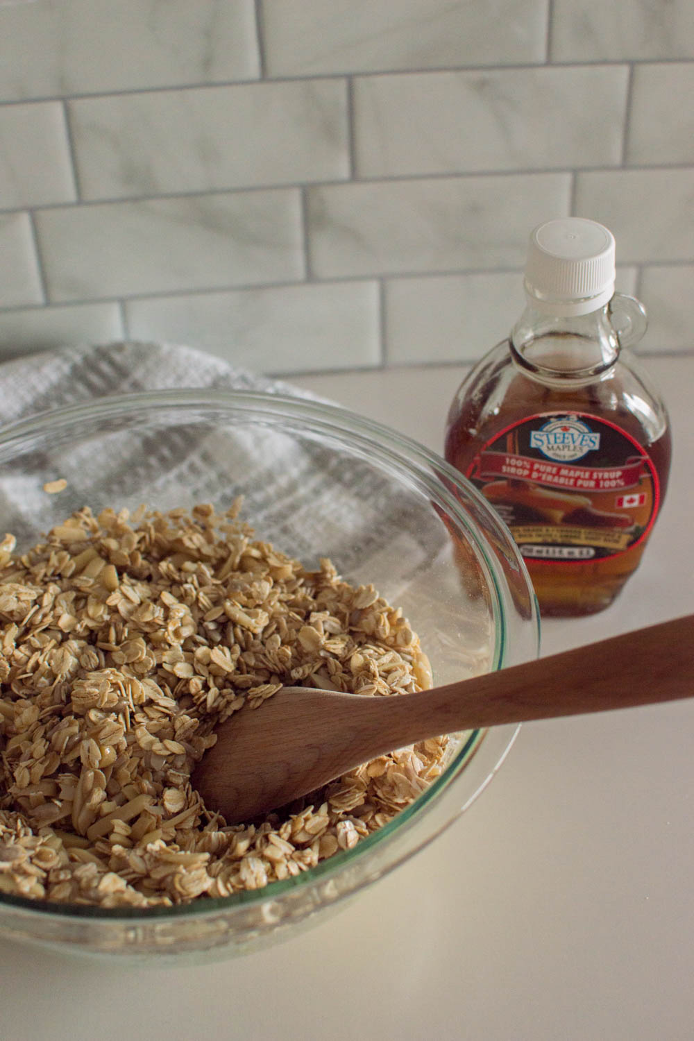 Using a wooden spoon to mix maple syrup into a granola mixture to make easy granola at home