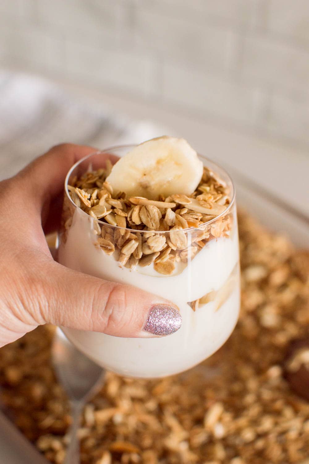 A hand holding a serving of yogurt and banana with homemade granola on top