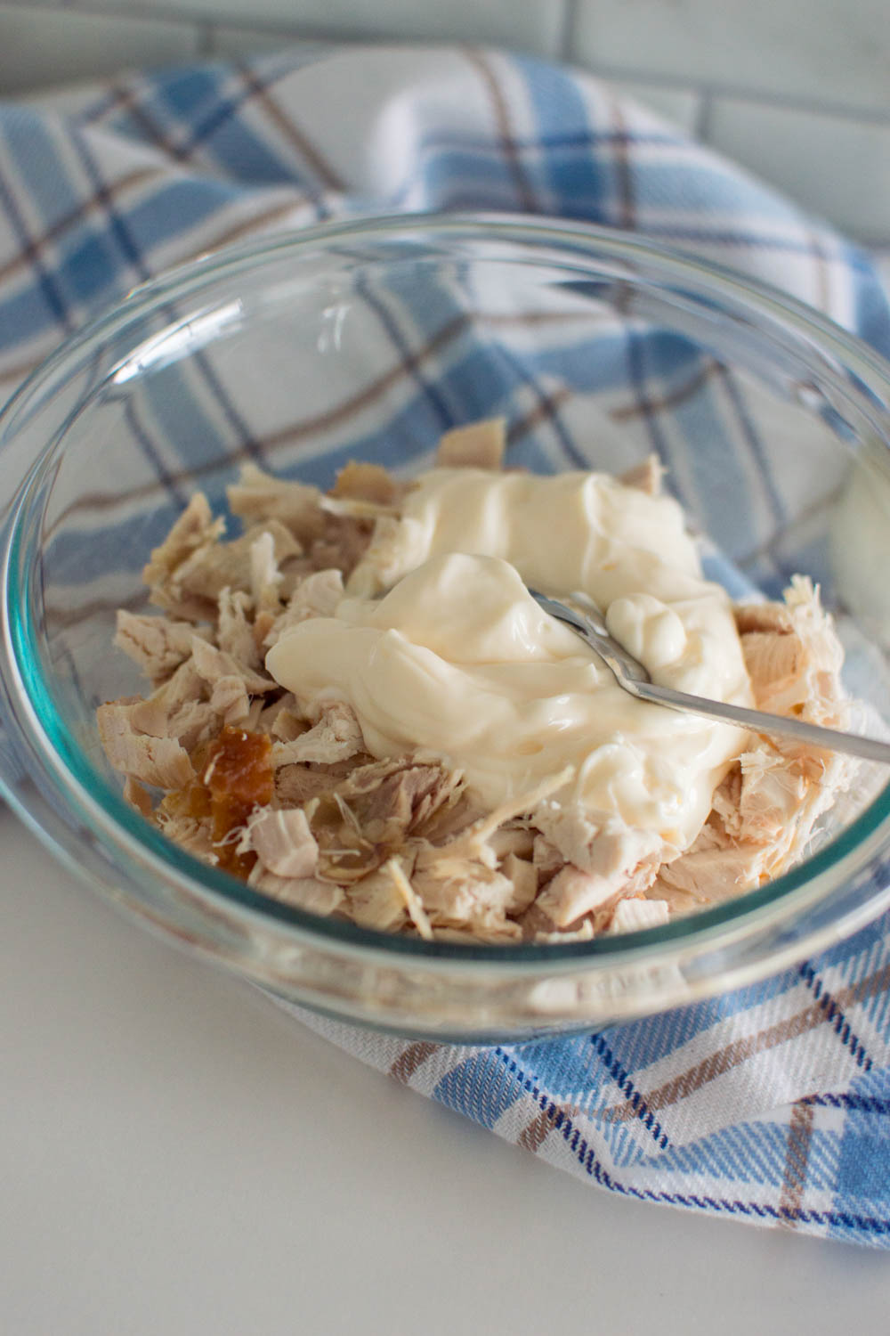Adding mayonnaise to chopped chicken in a glass bowl, mixed with a spoon