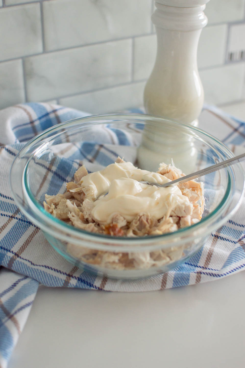 Adding mayonnaise to chopped chicken in a glass bowl, mixed with a spoon