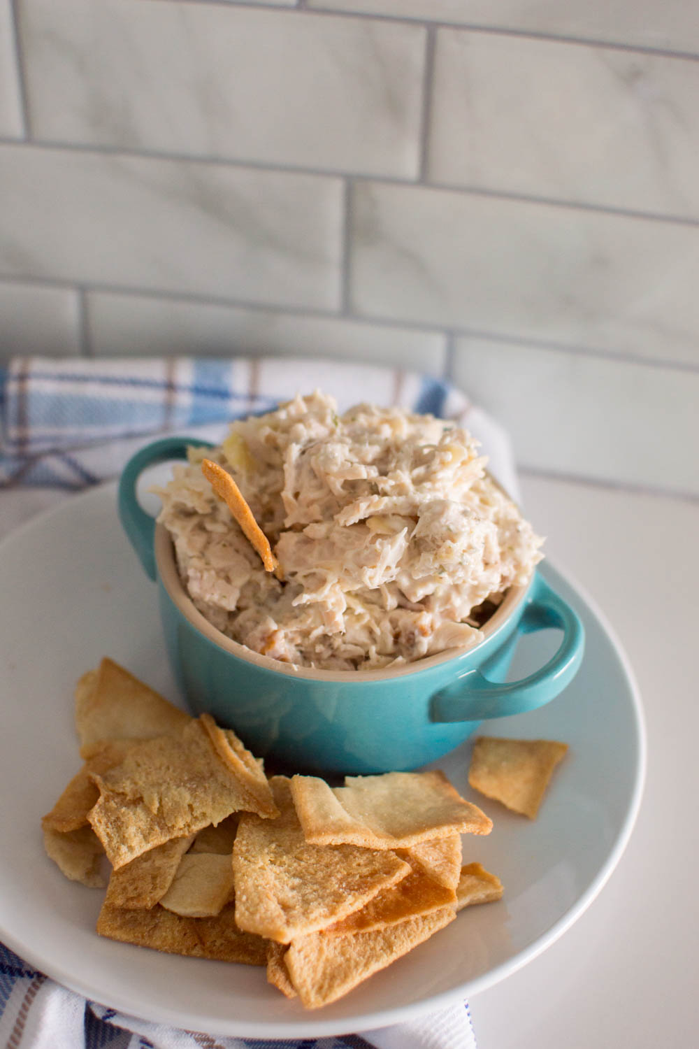 Chicken salad in a turquoise bowl, on a white plate and surrounded by pita chips