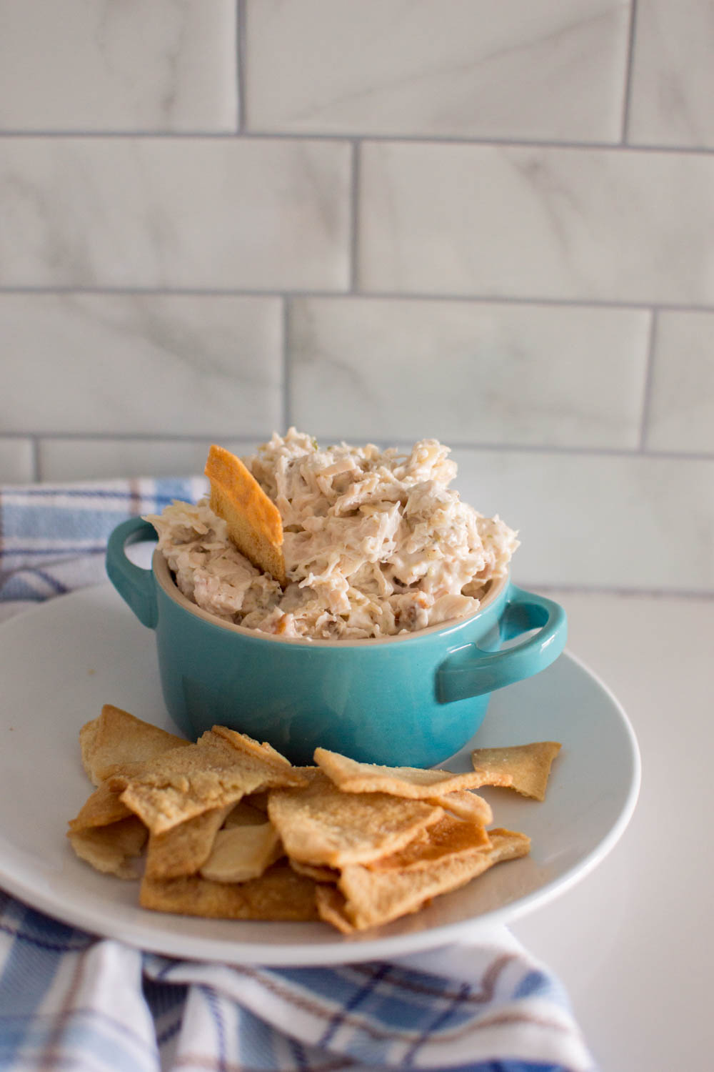 Chicken salad in a turquoise bowl, on a white plate and surrounded by pita chips