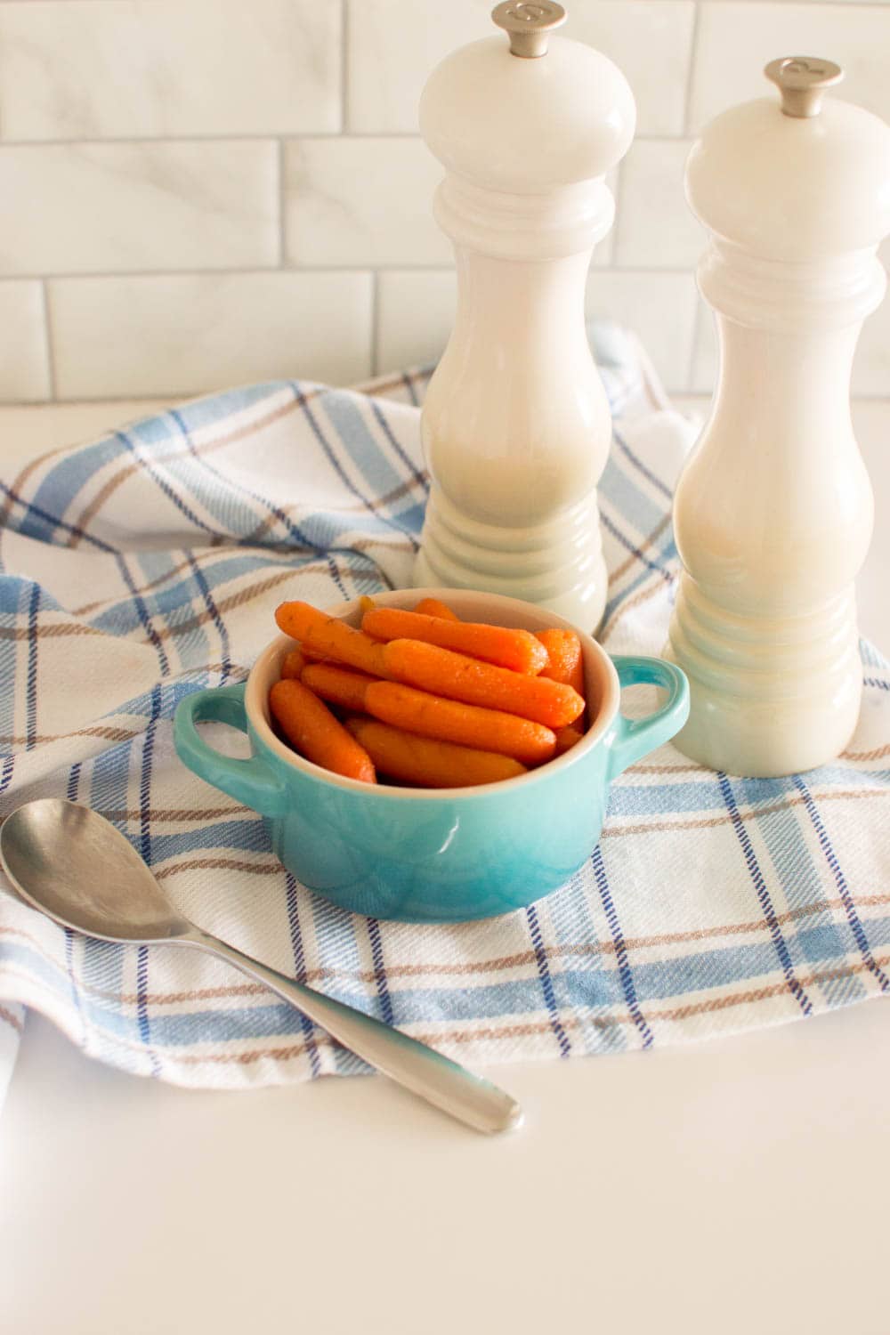 Our honey glazed baby carrots served in a turquoise bowl, with a spoon and salt and pepper shakers on the side