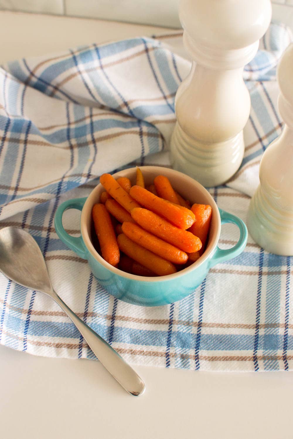Our honey glazed baby carrots served in a turquoise bowl, with a spoon and salt and pepper shakers on the side
