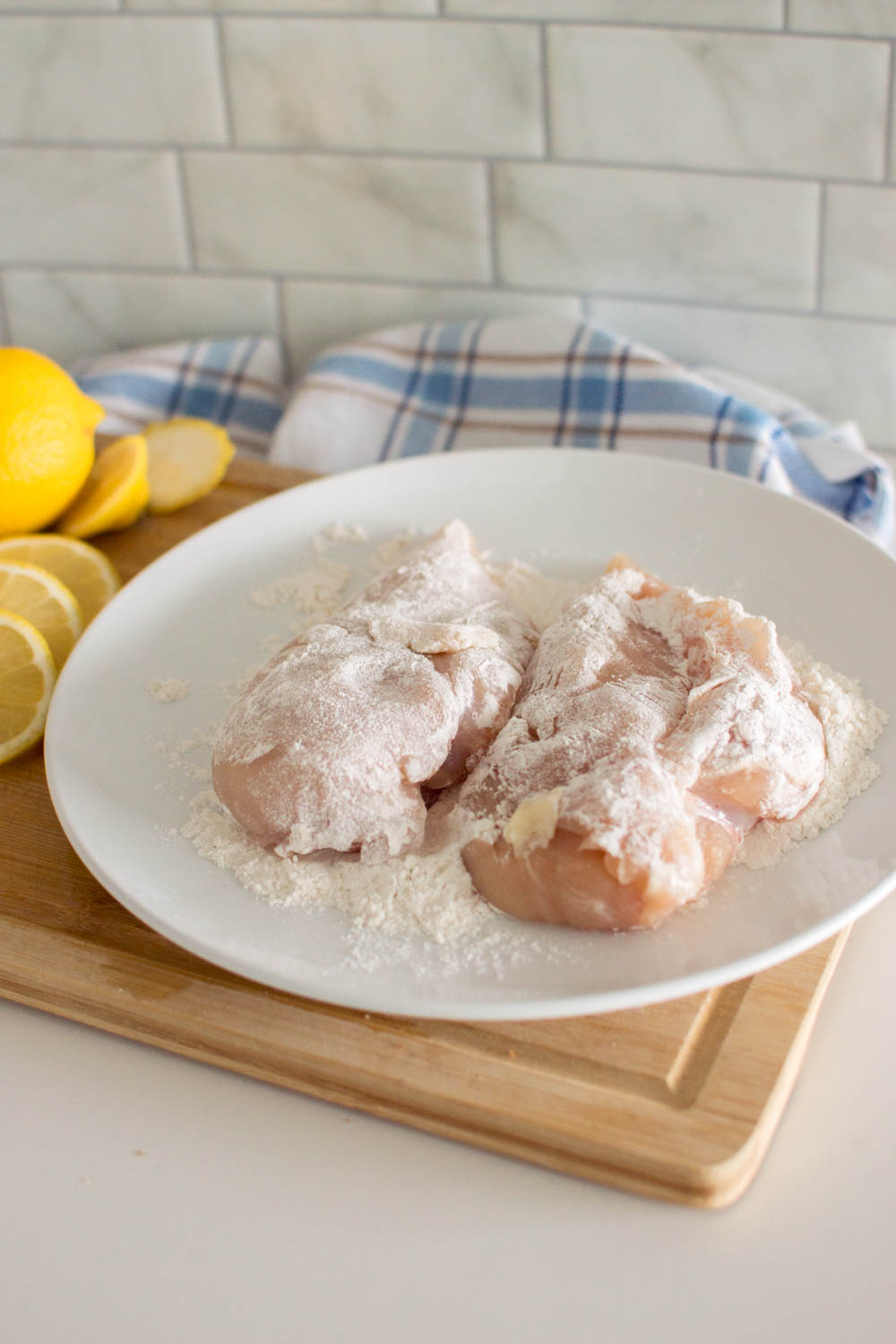 Floured raw chicken breasts sitting on a white plate