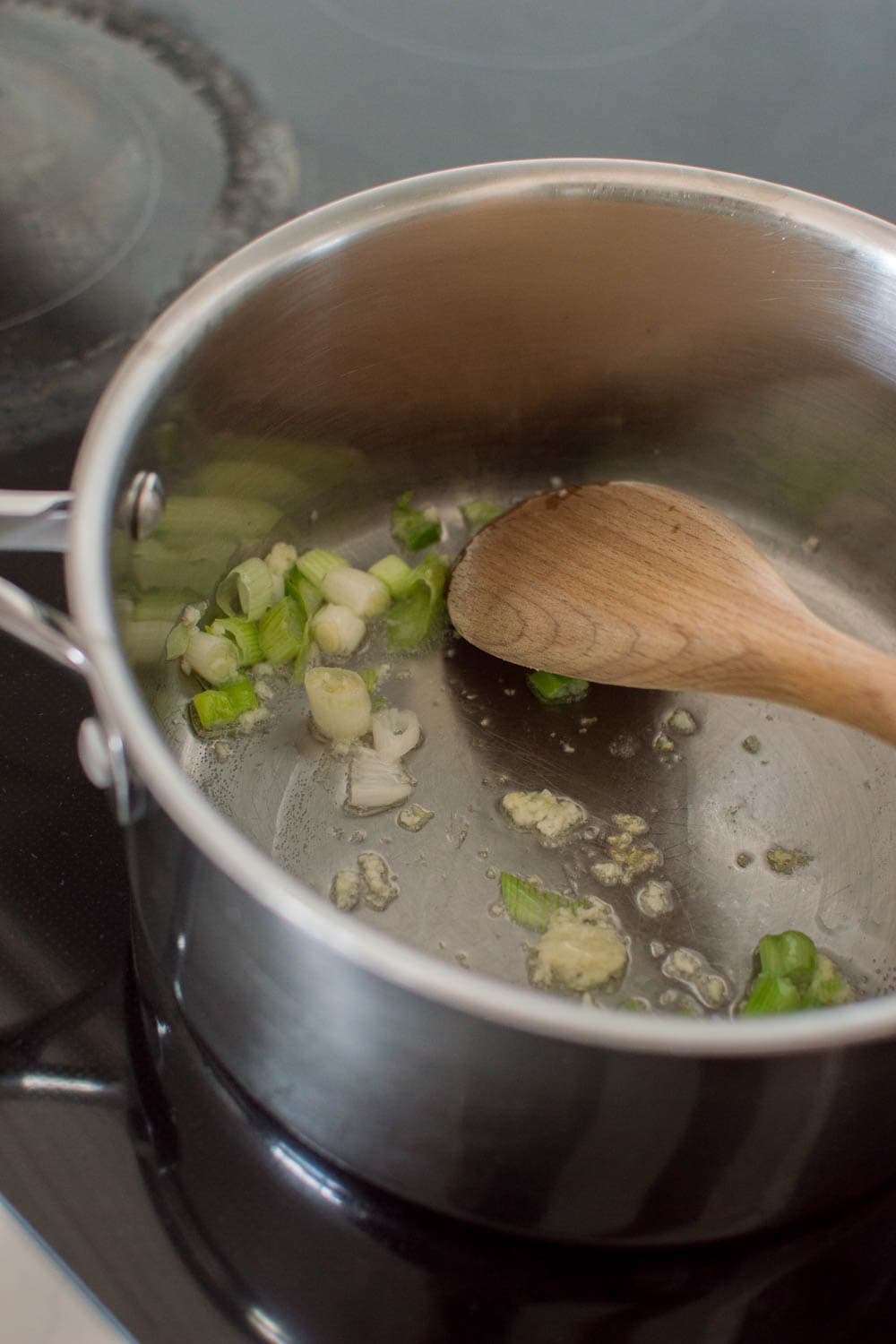 Simmering oil and green onions in a large saucepan, and mixing with a wooden spoon