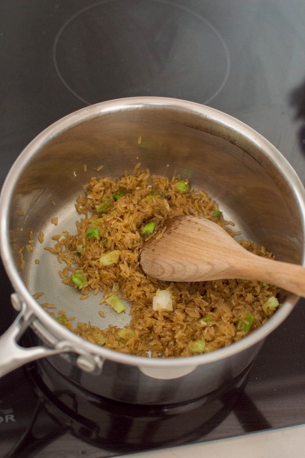 Roasting rice with oil and green onions in a large saucepan, and mixing with a wooden spoon