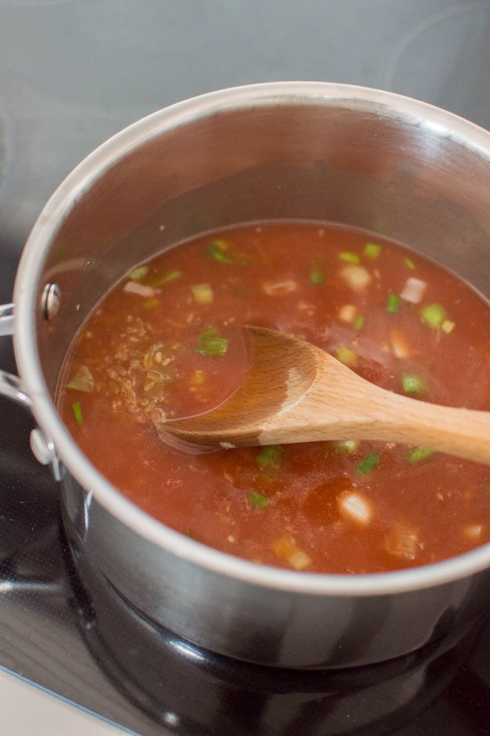 Adding broth and tomato sauce in a saucepan to make Mexican Rice