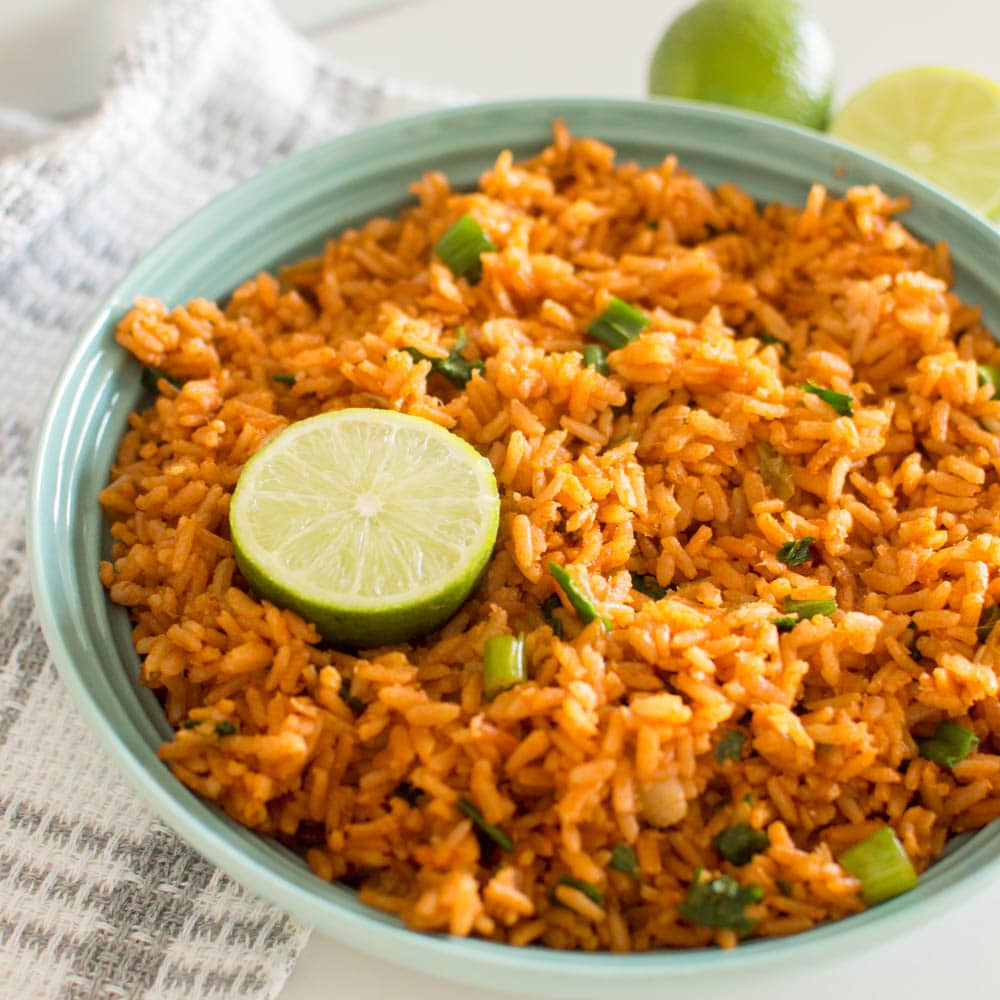 Our recipe for Easy Mexican Rice in a mint green bowl, served with a slice of fresh lime