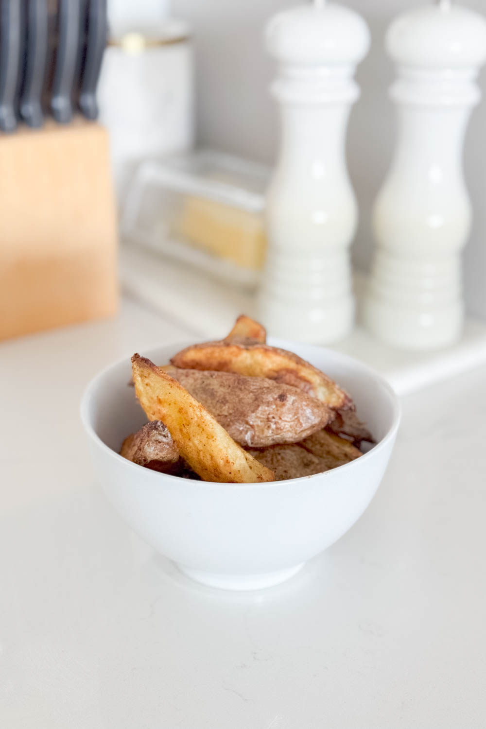 Homemade potato wedges in a white bowl, sitting on a marble counter