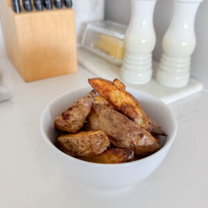 Homemade potato wedges in a white bowl, sitting on a marble counter