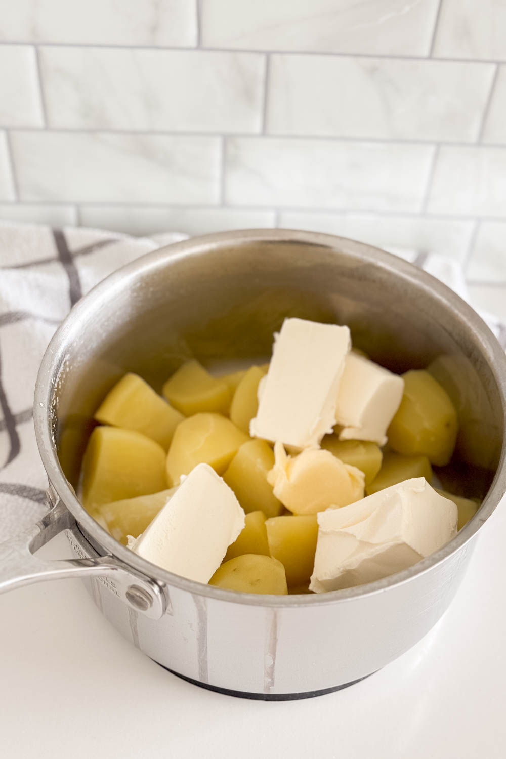 Adding cream cheese and milk into a pot of boiled potatoes