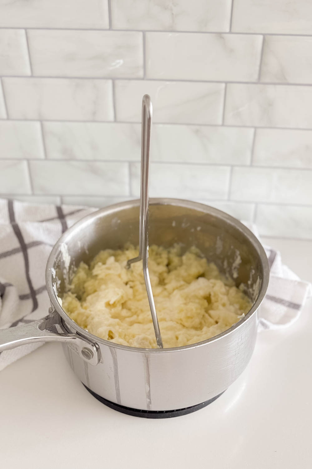 Using a potato masher to make mashed potatoes in a large pot