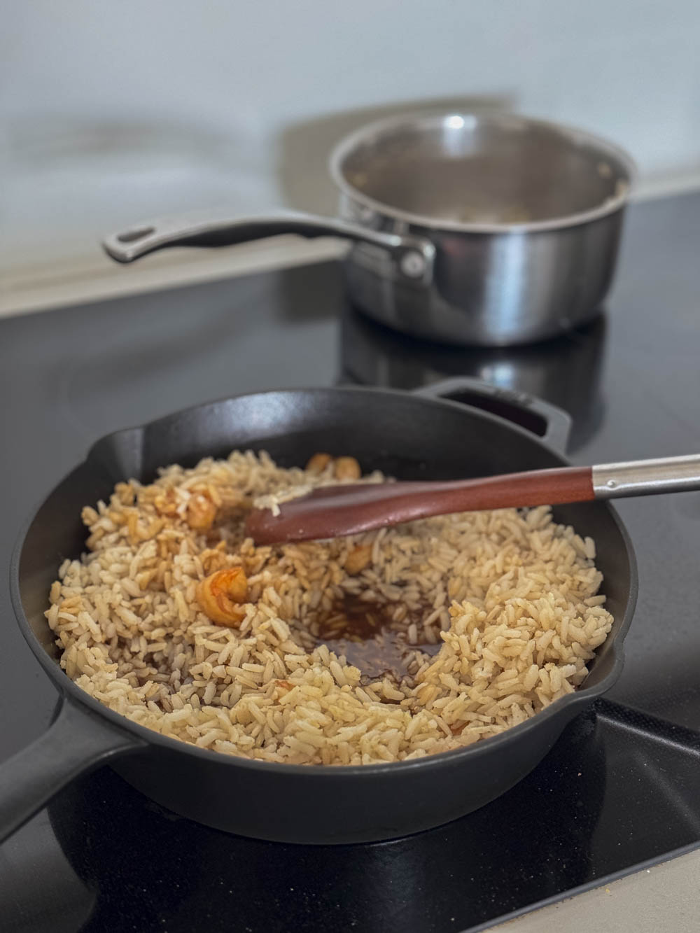 Adding brown rice to shrimp stir fry, being cooked in a cast iron skillet