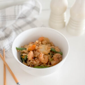 Easy shrimp stir fry served in a white bowl, accompanied by a tea towel, chop sticks and salt and pepper shakers