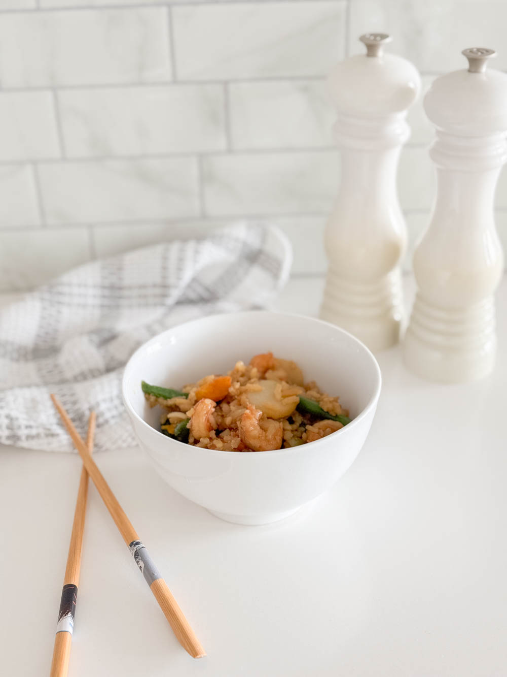 Easy shrimp stir fry served in a white bowl, accompanied by a tea towel, chop sticks and salt and pepper shakers