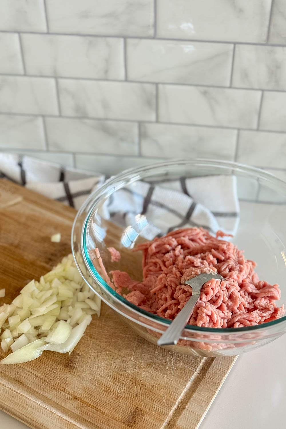 Raw ground turkey in a glass bowl, sitting on a wooden cutting board with some chopped onion